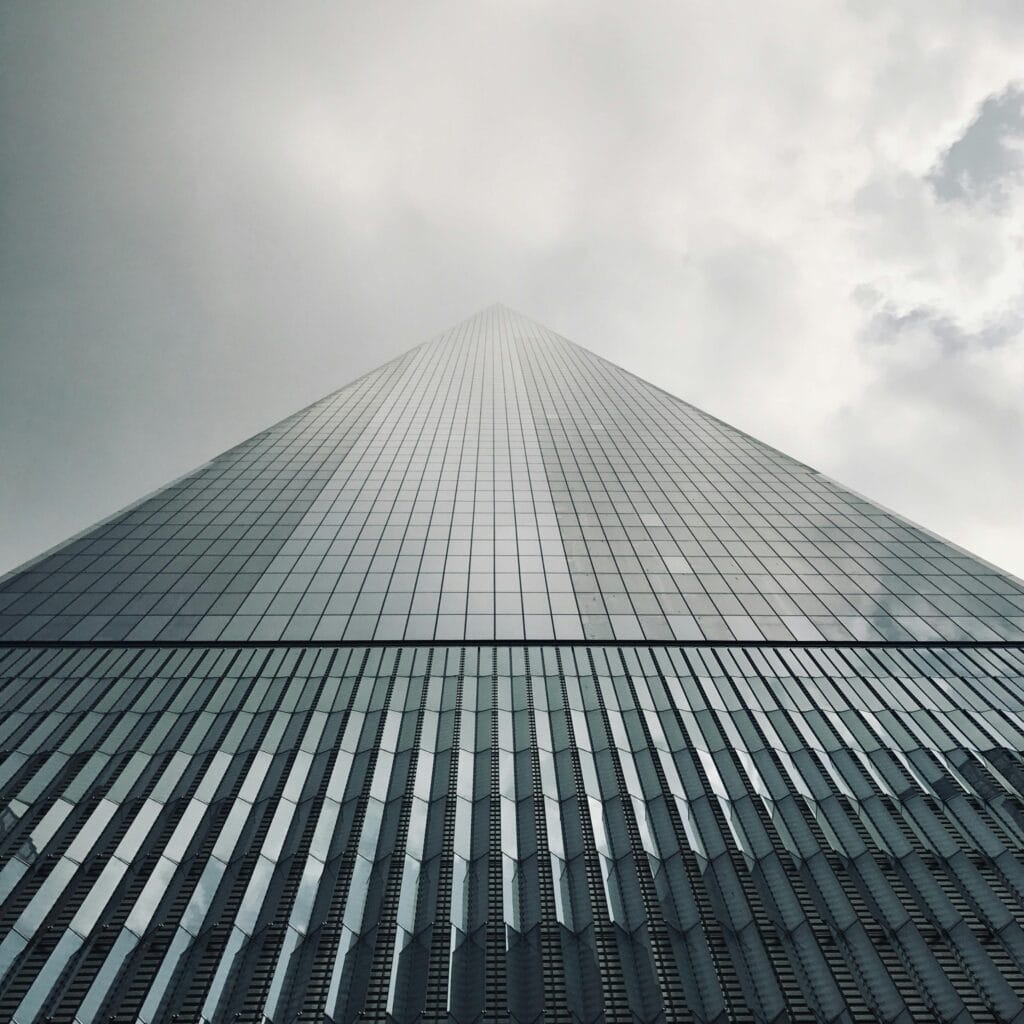 A dramatic low angle shot of One World Trade Center against cloudy skies in New York City.