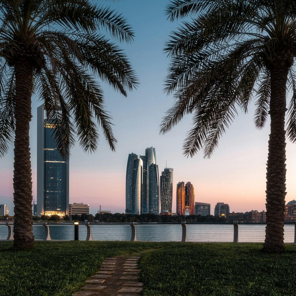 Beautiful Abu Dhabi cityscape at dusk with skyscrapers framed by palm trees and a tranquil water view.
