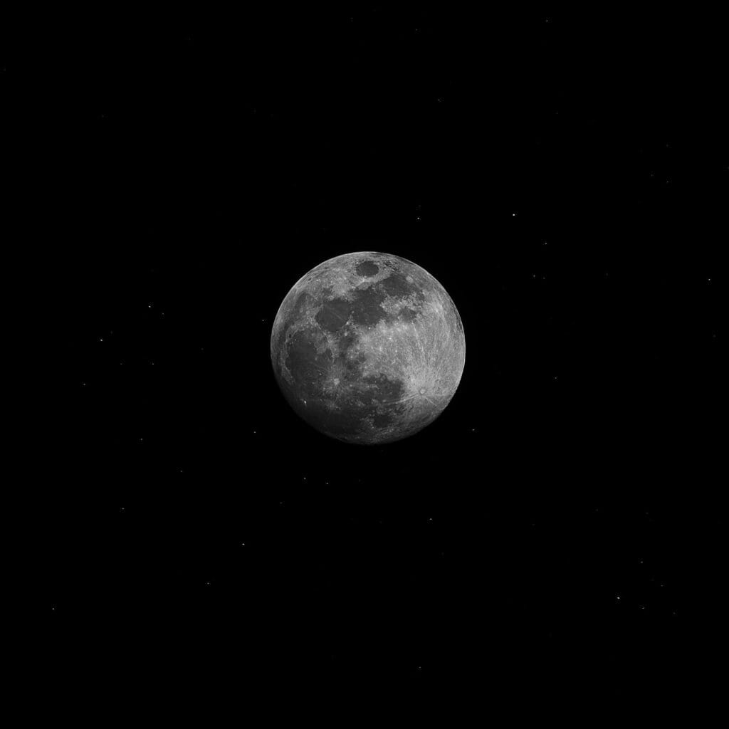 A captivating black and white photo of the full moon against a starry night sky.